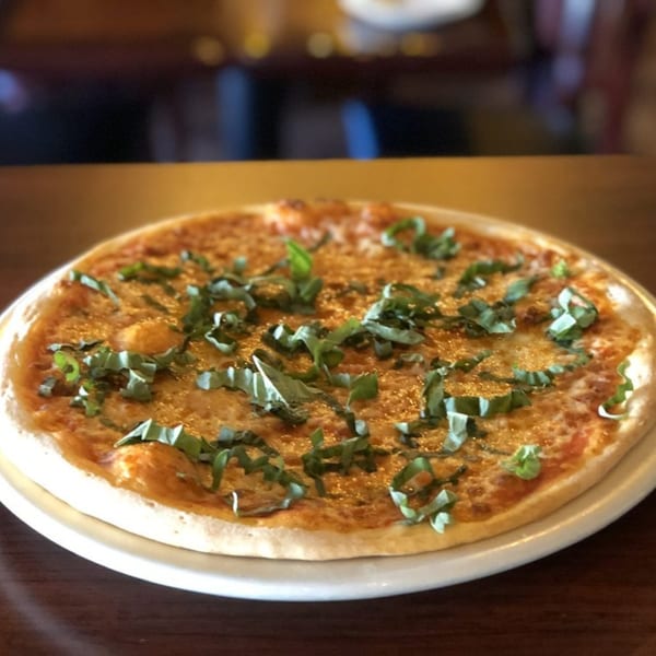 A freshly baked Italian pizza with melted cheese and basil leaves on a white plate.