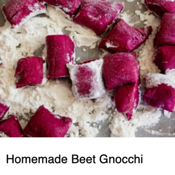 Uncooked, vibrant magenta beet gnocchi dusted with flour on a baking sheet, ready for cooking.