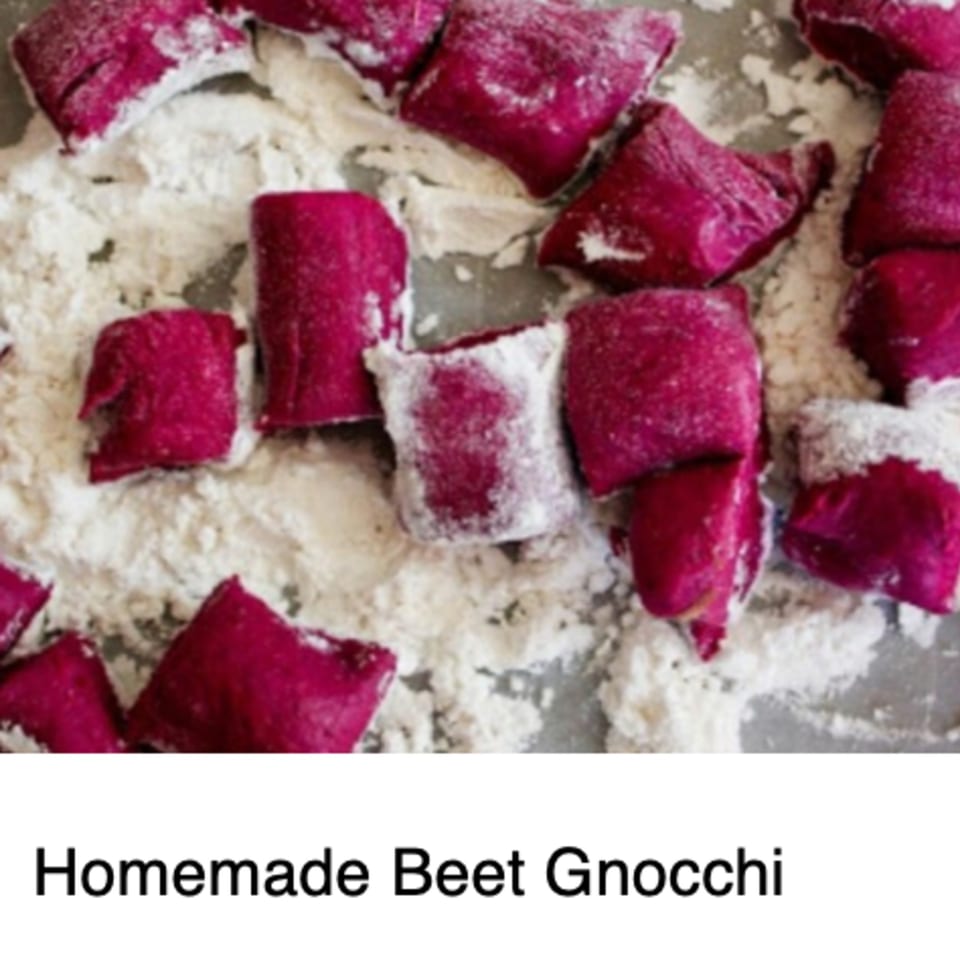 Uncooked, vibrant magenta beet gnocchi dusted with flour on a baking sheet, ready for cooking.