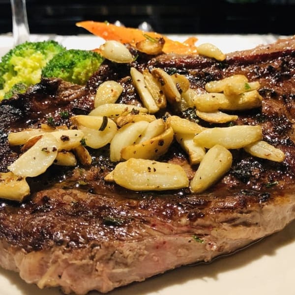 Grilled steak topped with roasted garlic cloves, served with broccoli and carrots.