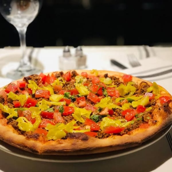 A Michelangelo Ristorante pizza with ground meat, diced tomatoes, and yellow peppers on a white tablecloth.