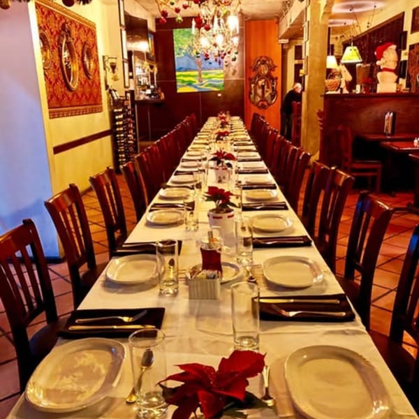 Long dining table set for many guests with white tablecloths, plates, and red poinsettia centerpieces.