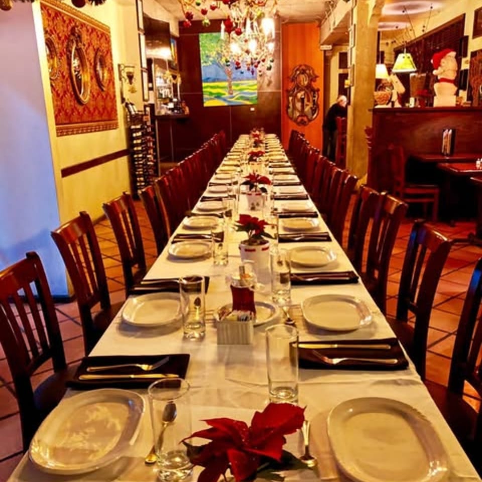 Long dining table set for many guests with white tablecloths, plates, and red poinsettia centerpieces.