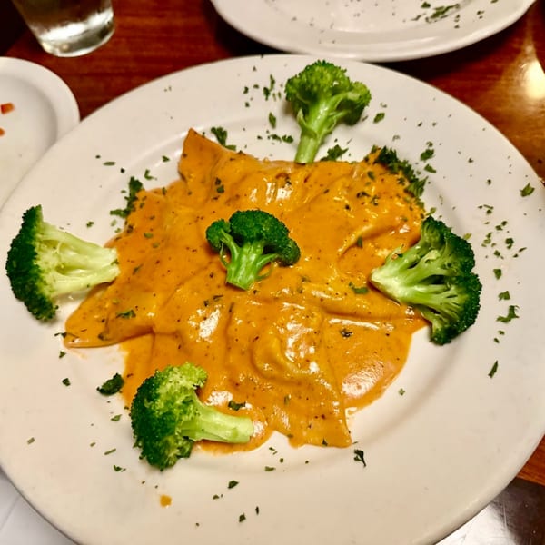 Italian pasta dish with orange sauce, garnished with fresh broccoli florets and parsley on a white plate.