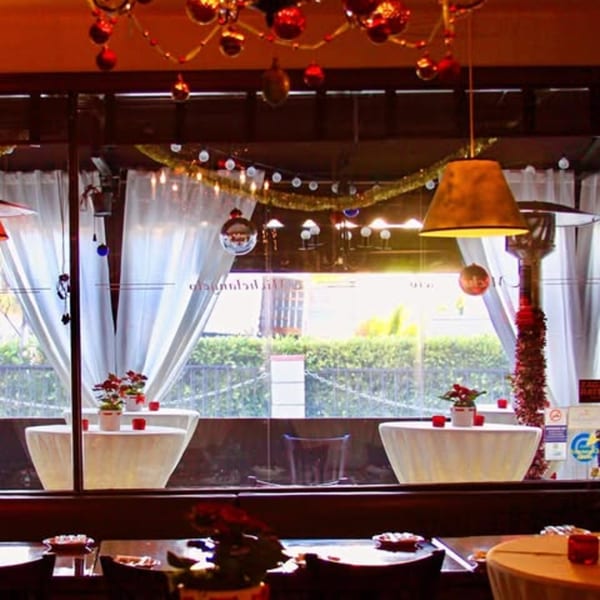 Restaurant interior with festive decorations, white draped tables by windows, and a warm ambiance.