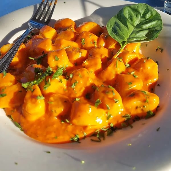 Gnocchi in a creamy orange sauce, garnished with fresh basil and parsley, with a fork.