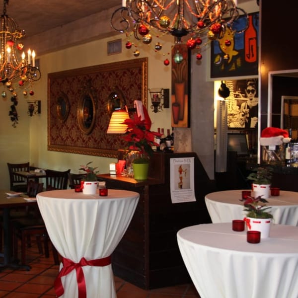 Festively decorated Italian restaurant interior with high-top tables, chandeliers, and Christmas ornaments.