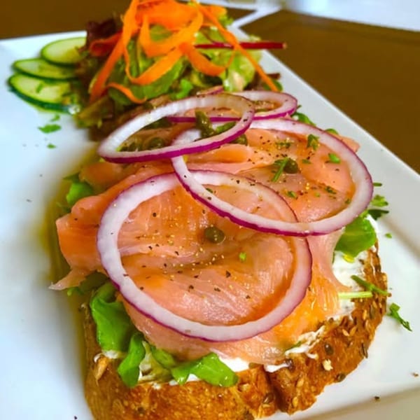 Smoked salmon and red onion on toast with a side salad of mixed greens and cucumbers.