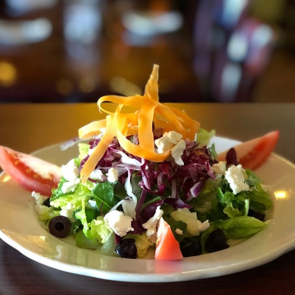 Fresh Italian garden salad with mixed greens, feta, olives, tomatoes, and carrot ribbons.