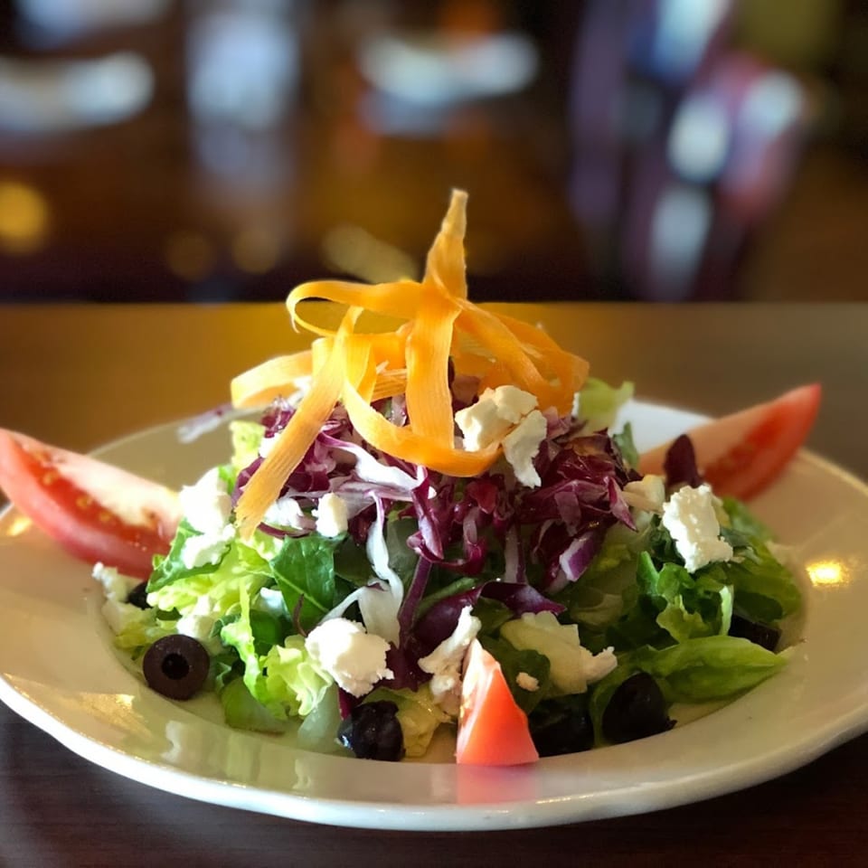 Fresh Italian garden salad with mixed greens, feta, olives, tomatoes, and carrot ribbons.