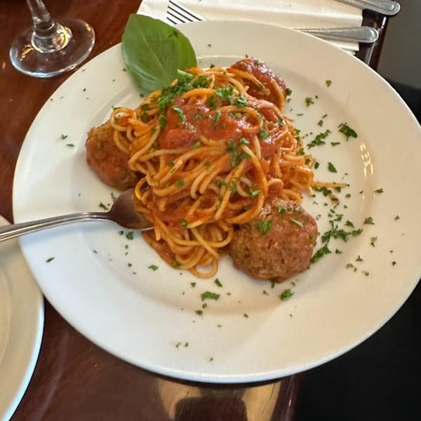 Spaghetti with meatballs and tomato sauce, garnished with fresh basil and parsley on a white plate.