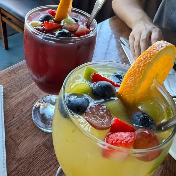 Two glasses of sangria, one red and one yellow, filled with fruit on a wooden table.