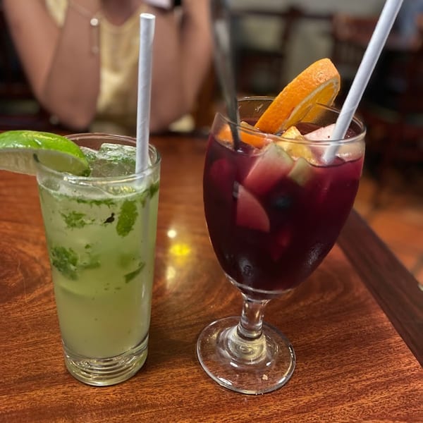 Two drinks, a green mojito and a red sangria with fruit, on a wooden table.