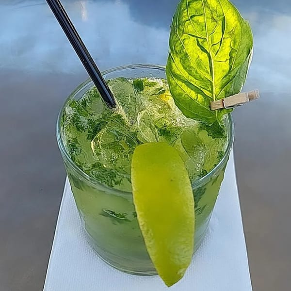 A vibrant green cocktail with ice, a black straw, a lime wedge, and a basil leaf.