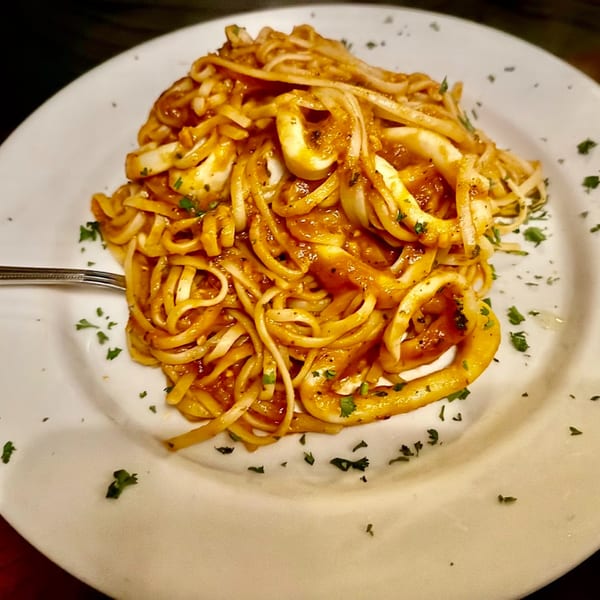 Linguine pasta with calamari and red sauce, garnished with parsley on a white plate.